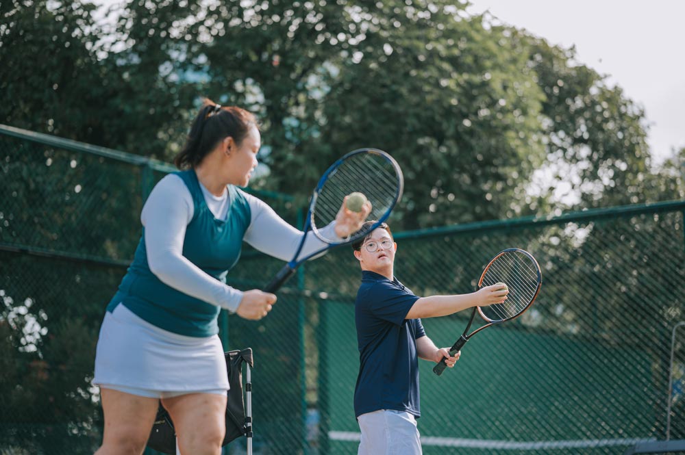 Asian Chinese Down syndrome man learning from trainer how to play tennis